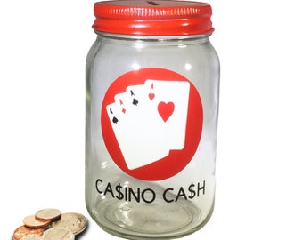 May include: A glass jar with a red lid and a red circle with four playing cards, including an ace of hearts, an ace of spades, an ace of clubs, and an ace of diamonds. The text "CASINO CASH" is printed on the jar.