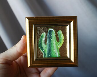 Peut inclure: Une petite peinture encadrée d'un cactus vert sur fond doré.