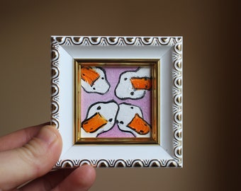 May include: A framed painting of four white ducks with orange beaks on a pink background.