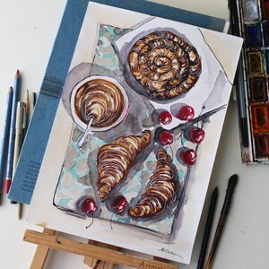 May include: Watercolor painting of a breakfast scene with a cup of coffee, two croissants, and a swirl of pastry. There are also red cherries scattered around the plate. The painting is on a white background with a blue border.