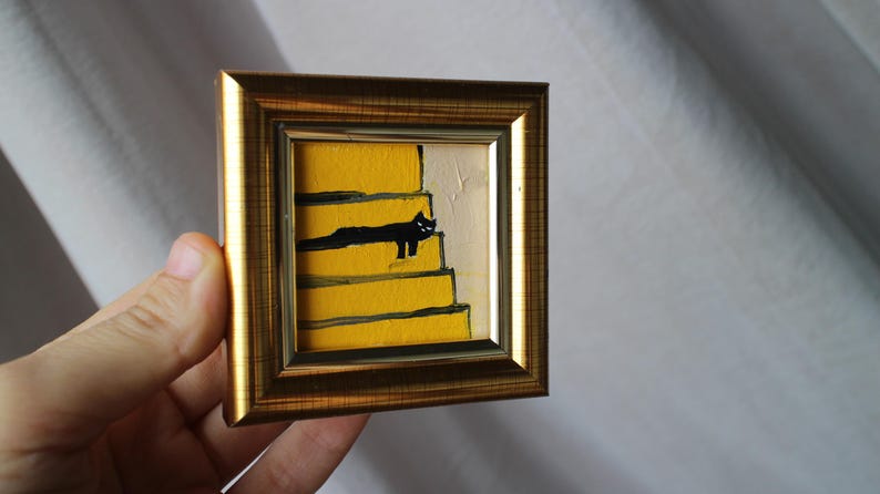 May include: A framed painting of a black cat sitting on yellow stairs. The painting is in a gold frame.