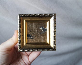 May include: A small, gold-framed picture with a black and white illustration of two dogs running. The frame has a decorative, ornate design.