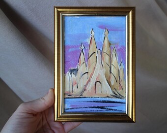 May include: A framed painting of a stylized cityscape with tall, pointed buildings in shades of beige and yellow against a purple and blue sky. The buildings are painted with thick brushstrokes, giving the painting a textured look.