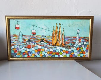 May include: A framed painting of a colorful cityscape with a blue sky and red cable cars. The cityscape features a tall building and a group of orange buildings with pointed roofs. The bottom of the painting features a mosaic of colorful stones.