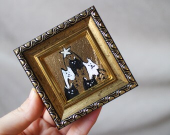 May include: A gold-framed painting of a black and white cat Christmas tree with a star on top. The painting is on a white background.