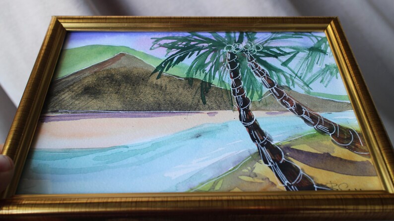 May include: Watercolor painting of a tropical beach scene with two palm trees in the foreground and a mountain in the background.
