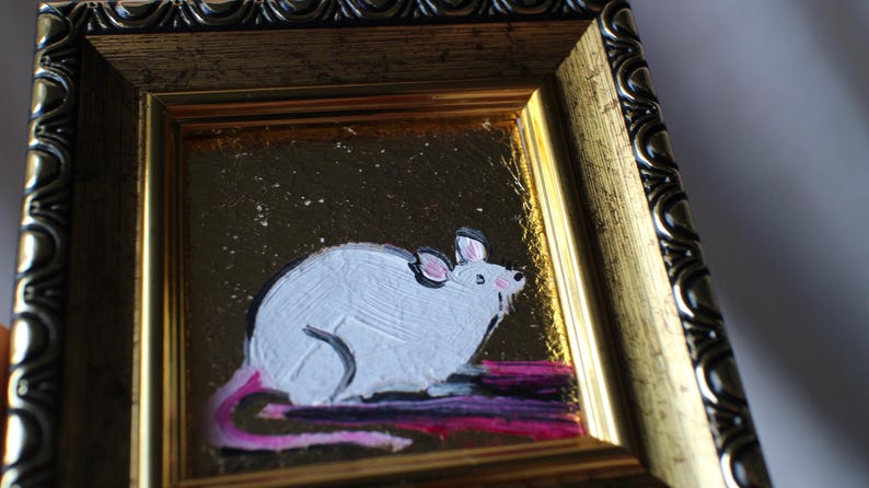 May include: A white mouse with a pink tail is painted on a gold background with a sparkly texture. The painting is framed in a gold and black ornate frame.