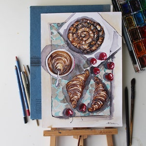 May include: Watercolor painting of a still life featuring a cup of coffee, two croissants, and a plate of cherries. The painting is on a blue background with a white border.