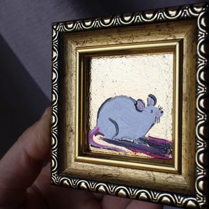 May include: A small framed painting of a gray mouse with a pink tail on a gold background.