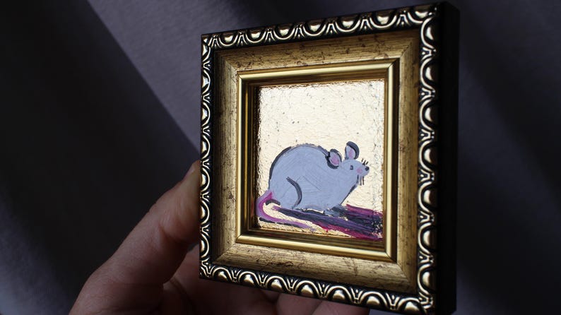 May include: A small framed painting of a gray mouse with a pink tail on a gold background.