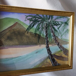 May include: A framed watercolor painting of a tropical scene with two palm trees in the foreground and a mountain in the background. The painting is done in shades of blue, green, and brown.