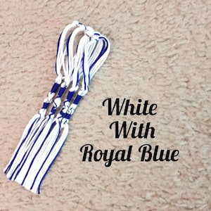 May include: Three white and royal blue tassels are displayed against a textured, light brown background. The tassels are knotted at the top and have a series of royal blue accents. The text "White With Royal Blue" is visible in the image.
