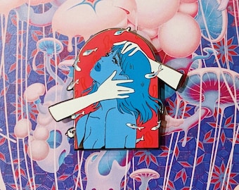 May include: A metal enamel pin featuring a blue-skinned figure with blue hair inside a red arched frame. Two pale hands reach into the frame to touch the figure's head and face. Small white fish swim around the figure against the red background.