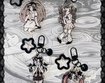 May include: Four acrylic keychains featuring black and white anime-style character illustrations. Each charm includes a black star-shaped clasp and a small black bead. The designs depict various figures with distinct hairstyles and outfits.