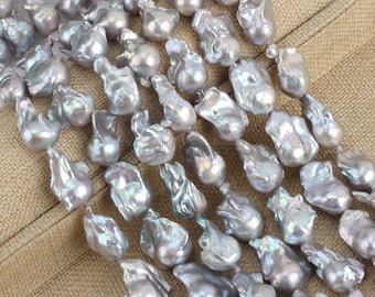 May include: A selection of irregularly shaped, iridescent grey pearls. The pearls have a unique, organic form, with a smooth, lustrous surface. The pearls are strung together, suggesting they are for jewellery making or crafting.