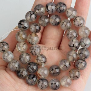 May include: A strand of grey and black agate beads with a crackled texture. The beads are round and have a translucent appearance.