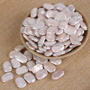 Puede incluir: Una colección de perlas iridiscentes, de color blanquecino, de forma irregular, algunas de las cuales se derraman de un cuenco marrón. Las perlas tienen un brillo lustroso y una forma orgánica ligeramente aplanada. El texto "AndyDIYpearl4U" es visible.