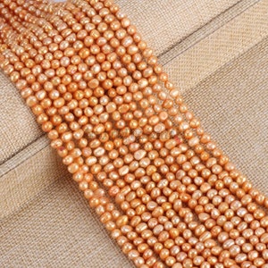 Peut inclure: Plusieurs rangées de perles d'eau douce de couleur pêche. Les perles sont petites, rondes et ont un fini brillant. Elles sont enfilées, créant un aspect élégant. Le fond est beige neutre.