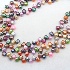 Puede incluir: Una colección de perlas multicolores de forma irregular en tonos rosa, verde, naranja y morado. Las perlas están ensartadas, creando un diseño de collar o pulsera. Las perlas tienen un brillo lustroso.