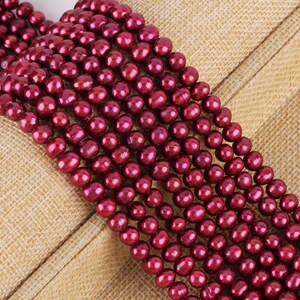 以下が含まれることがあります： 深紅色の真珠の複数のストランドのクローズアップ。真珠は丸く、光沢のある虹色の仕上がりです。ビーズは、ニュートラルな質感の背景に表示されます。ジュエリー作りに最適です。