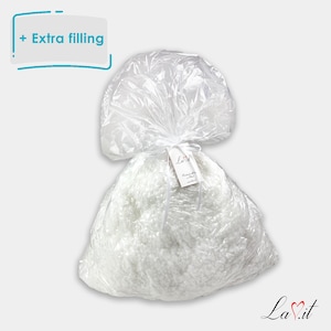 May include: A clear plastic bag filled with white, fluffy stuffing material. The bag is gathered at the top with a white ribbon and features a small white tag with the text La.it. A graphic in the top left corner displays the text + Extra filling.