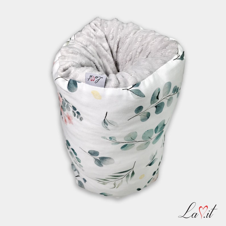 May include: A cylindrical fabric sleeve featuring a white exterior with a watercolour eucalyptus leaf pattern in shades of green and soft pink. The interior is lined with a textured, light grey plush fabric. A small tag reads La.it.