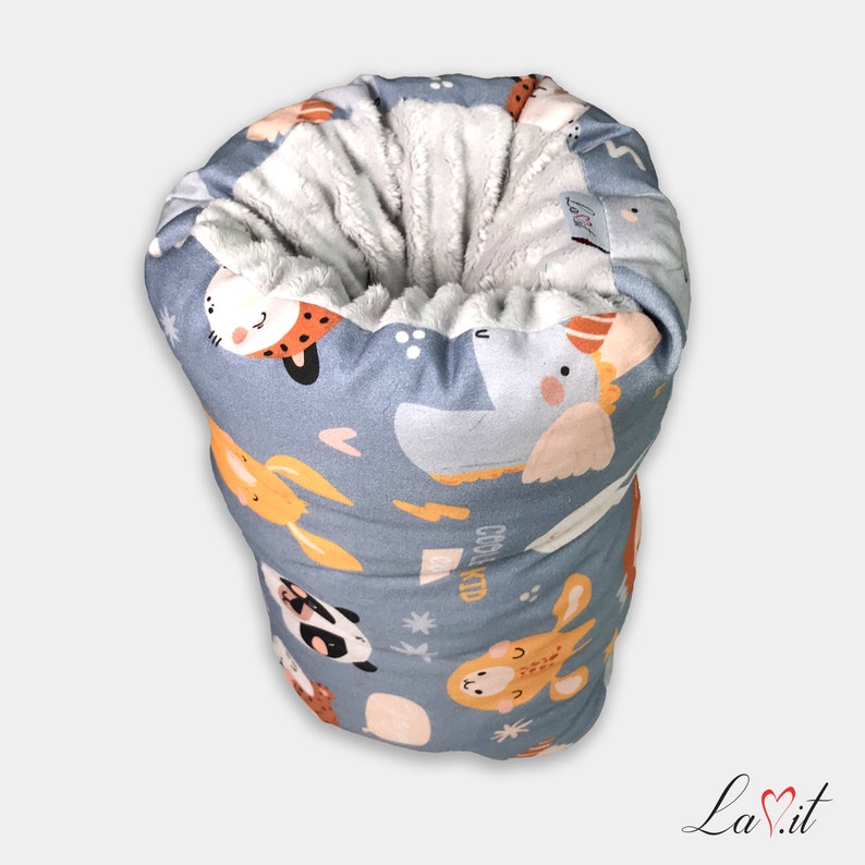 May include: A cylindrical fabric sleeve featuring a light blue exterior with a repeating pattern of cartoon animals, including a panda, giraffe, and elephant, alongside small stars and hearts. The interior is lined with a soft, white, textured plush fabric.