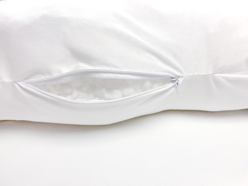 Pode incluir: Uma fronha retangular branca com um fecho de correr horizontal na lateral. O fecho est&aacute; parcialmente aberto, revelando um vislumbre do material de enchimento branco, texturizado e macio contido no interior da almofada.