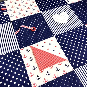 May include: A blue and white baby play mat with different textures and patterns. The mat features a white heart, red and white gingham fabric, and a blue and white striped fabric. The mat is perfect for babies to explore and learn.