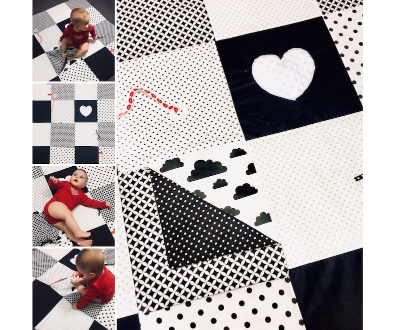 May include: Black and white baby play mat with different textures and patterns. The mat features a large white heart, polka dots, geometric shapes, and clouds. A baby is playing on the mat.