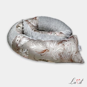 Peut inclure: Un oreiller de grossesse gris et beige à motifs avec un tissu gris doux d'un côté. L'oreiller est en forme de beignet et est conçu pour soutenir le corps pendant la grossesse.