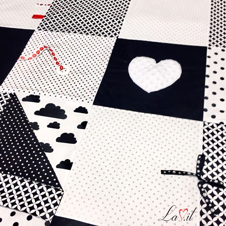 May include: Black and white baby play mat with different textures and patterns, including polka dots, clouds, and a heart. The mat is made of soft fabric and is perfect for babies to explore and learn.