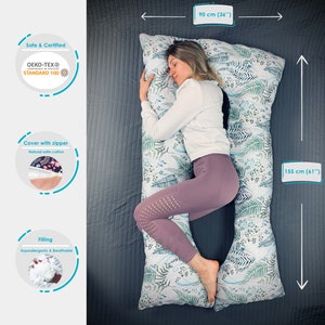 May include: A U-shaped body pillow with a white cover featuring a green and blue fern leaf pattern. The pillow measures 36 inches wide by 61 inches long. It includes a zipper closure, OEKO-TEX Standard 100 certification, and hypoallergenic filling.