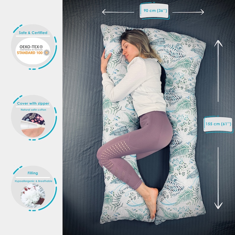 May include: A U-shaped body pillow with a white cover featuring a green and blue fern leaf pattern. The pillow measures 36 inches wide by 61 inches long. It includes a zipper closure, OEKO-TEX Standard 100 certification, and hypoallergenic filling.