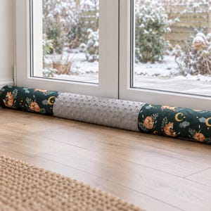 Peut inclure: Un boudin de porte cylindrique et long, composé d'un tissu vert foncé à motifs répétés de renards orange, de croissants de lune jaunes et de nuages gris, séparé par une section centrale en tissu minky gris clair texturé à pois.