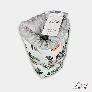 May include: A soft, grey, dimpled minky fabric blanket with a white exterior featuring a watercolour print of forest animals and green leaves. A white ribbon ties a rectangular tag to the top, displaying the text LaVit, Handmade with love in Poland.