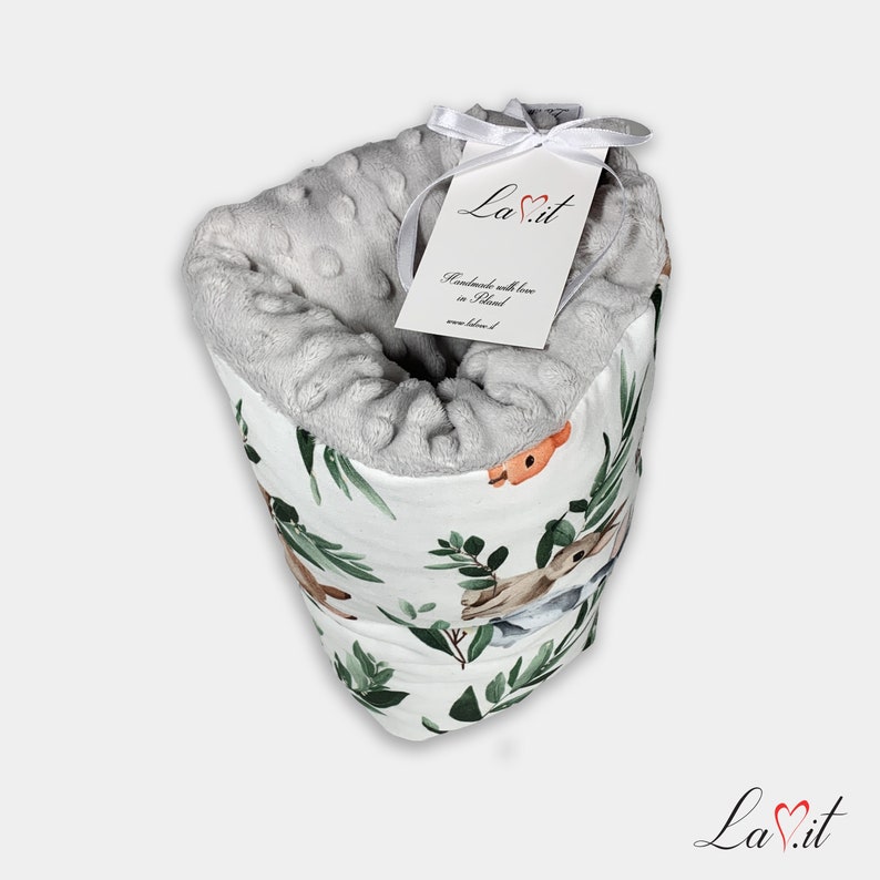 May include: A soft, grey, dimpled minky fabric blanket with a white exterior featuring a watercolour print of forest animals and green leaves. A white ribbon ties a rectangular tag to the top, displaying the text LaVit, Handmade with love in Poland.