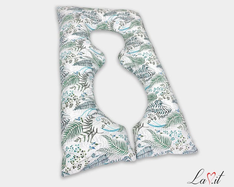 May include: A U-shaped body pillow featuring a white fabric base with a repeating botanical pattern of green fern leaves and small blue sprigs. The pillow has a distinct curved design with two long arms and a rounded top section for support.