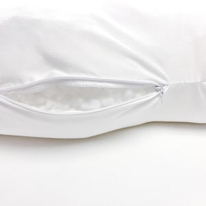 May include: A plain white pillowcase featuring a horizontal zipper closure along the side. The zipper is partially open, revealing the soft, white, textured polyester fiberfill stuffing inside the pillow. The fabric appears smooth and opaque.