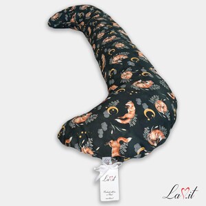 Pode incluir: Uma almofada de corpo longa e curva com um fundo verde escuro e um padr&atilde;o repetitivo de raposas cor de laranja, luas crescentes amarelas, nuvens cinzentas e ramos florais brancos. Uma etiqueta branca com o texto La.it est&aacute; presa por uma fita.