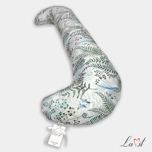 Pode incluir: Uma almofada de corpo longa e curva com fundo branco e uma estampa bot&acirc;nica de folhas de samambaia verdes e pequenas flores azuis. Uma etiqueta retangular branca com o texto La.it est&aacute; presa &agrave; extremidade inferior com uma fita.