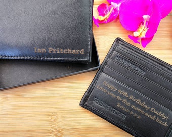 May include: Two black leather wallets with gold lettering. The top wallet has the name "Ian Pritchard" engraved on it. The bottom wallet has the text "Happy 40th Birthday Daddy! Love you to the moon and back" and "GENUINE LEATHER" engraved on it.