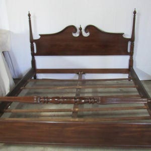 May include: A dark brown wooden four-poster bed frame. The headboard has a decorative, curved top. The bed frame has four tall posts with finials and a footboard. The bed frame is approximately 80 inches long.