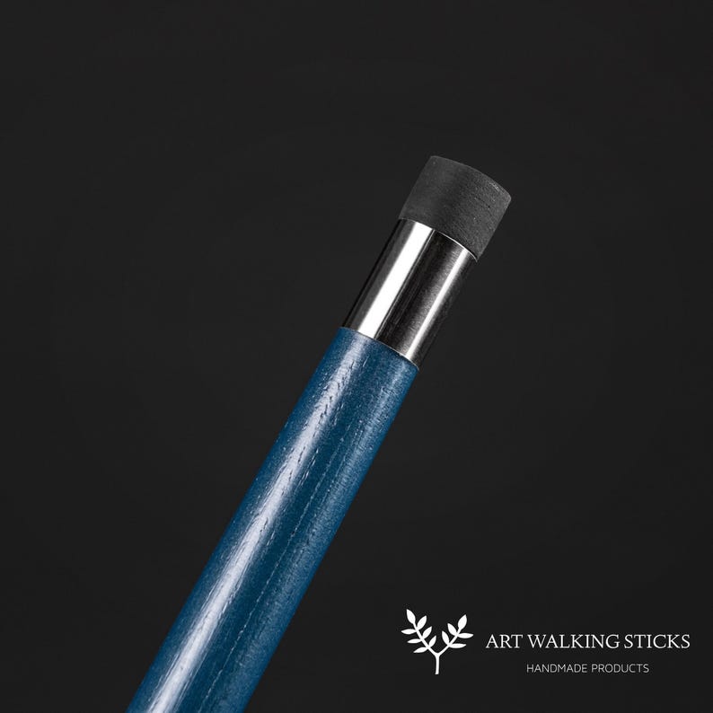 May include: Close-up of the top of a blue walking stick with a silver metal band and a black rubber tip. The stick is made of wood and has a smooth finish.