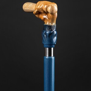 May include: A wooden walking stick with a hand holding a baseball bat. The hand and bat are carved from wood and painted in a natural wood tone. The stick is painted a dark blue color.