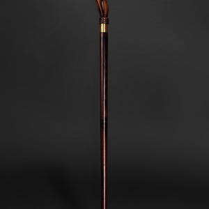 May include: A wooden walking stick with a detailed carved ram head handle. The stick is brown with a dark brown stain and has a gold metal tip.