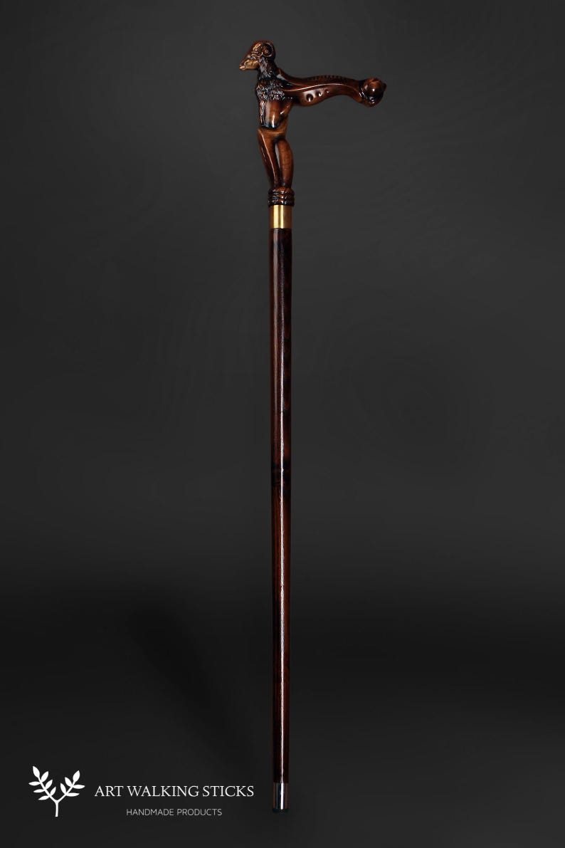 May include: A wooden walking stick with a detailed carved ram head handle. The stick is brown with a dark brown stain and has a gold metal tip.