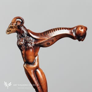 May include: A wooden walking stick with a carved ram head handle. The ram has a brown and gold finish and is intricately detailed. The stick is made by Art Walking Sticks, Handmade Products.