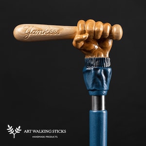May include: A wooden walking stick with a carved hand holding a baseball bat. The bat is inscribed with the word "Yankees". The stick is painted blue and has a silver metal tip.