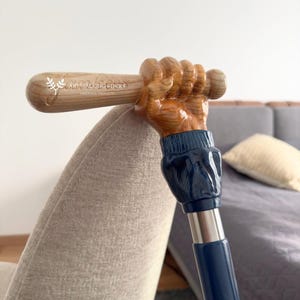 May include: A wooden walking stick with a carved hand holding a baseball bat. The bat is engraved with the text "Art Walking Sticks Handmade Products". The stick is painted blue and has a silver metal shaft.